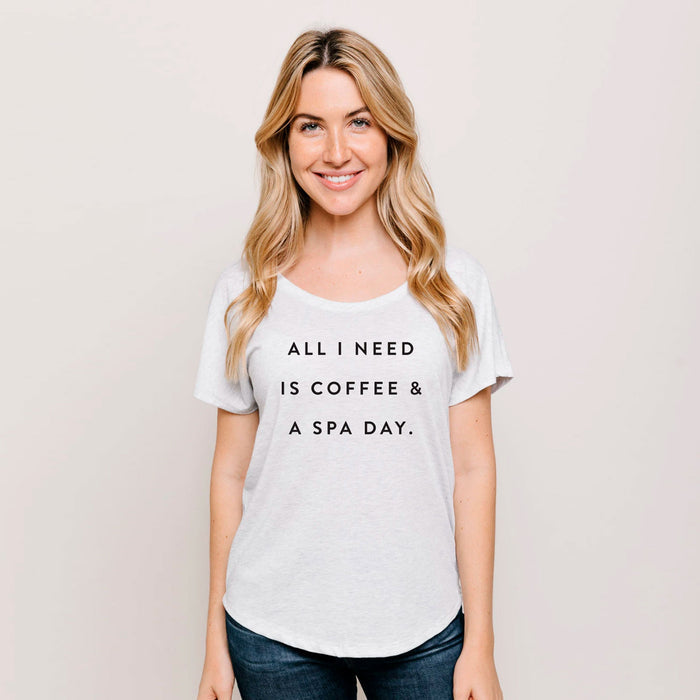 A smiling woman wearing a white Coffee & A Spa Day Women's T-Shirt | Lucky Owl with the phrase "All I need is coffee & a spa day" printed on the front, styled casually with jeans.